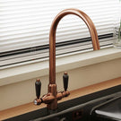 Copper-toned kitchen bridge style faucet.