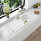 White kitchen sink with gold faucet on marble countertop