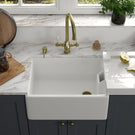 White farmhouse sink with gold faucet on a counter.
