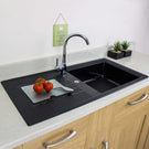 Black kitchen sink with tomatoes and a cutting board on a countertop.
