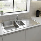 Stainless steel kitchen sink in a modern kitchen setting with a window and countertop.