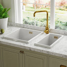 White double-basin sink with a gold kitchen faucet.