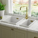 White double-basin kitchen sink with a gold-toned bridge style faucet.