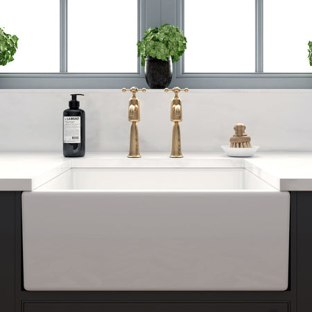 White ceramic kitchen sink with two gold single-lever faucets