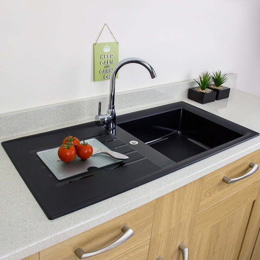 Black kitchen sink with tomatoes and a cutting board on a countertop.