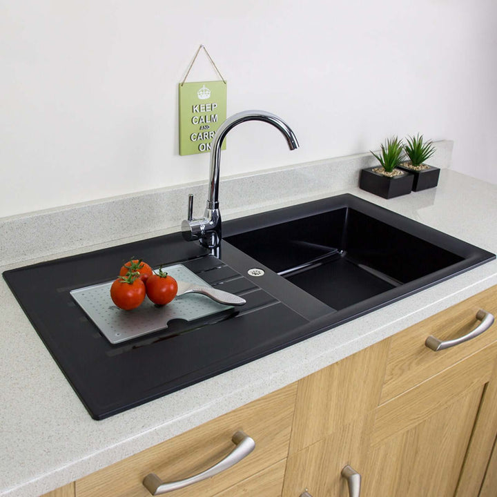 Black kitchen sink with tomatoes and a cutting board on a countertop.