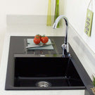 Black kitchen sink with a silver faucet and tomatoes on a white countertop.
