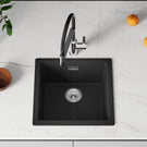 Black kitchen sink with faucet on a white countertop with fruits and a plant.
