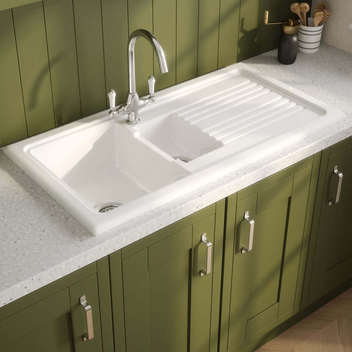 Green kitchen cabinets with a white sink and countertop.