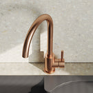 Rose gold kitchen faucet on a modern sink with a light gray backsplash.