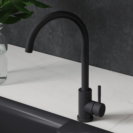 Black kitchen faucet over a black sink with oranges and a plant on a white countertop.