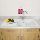Kitchen sink with vegetables and a knife on a white countertop, with a motivational sign in the background.