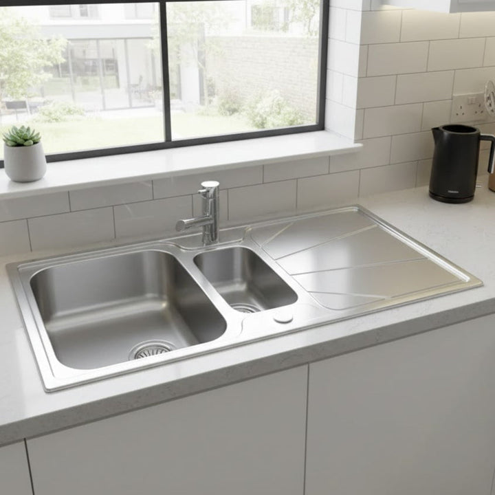 Stainless steel kitchen sink in a modern kitchen setting with a window and countertop.